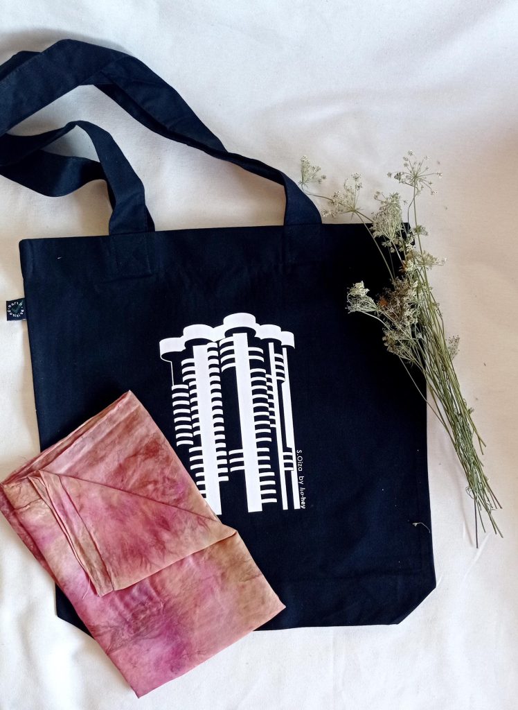 Tote bag negra con Torres Blancas serigrafiada en blanco, junto a un pañuelo rosa y flores secas
