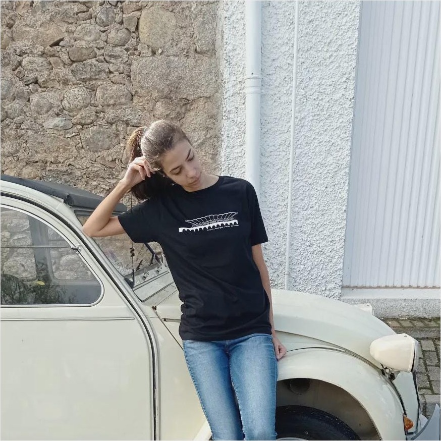 Chica apoyada en un coche clásico con camiseta negra estampada con la marquesina del Hipódromo de la Zarzuela